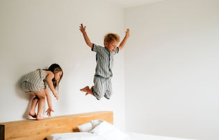 Twin toddlers jumping on a bed, showing signs of hyperactive behaviour and overtiredness before bedtime