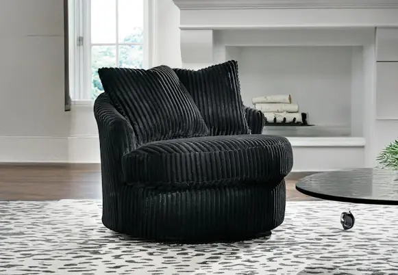 Modern black corduroy swivel accent chair with pillows on a rug.