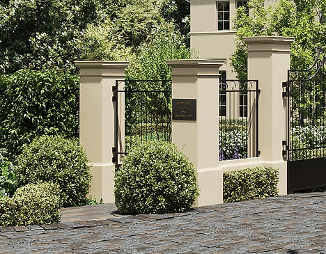 A grand estate entrance framed by lush greenery and a blooming white flowering tree. The driveway is elegantly paved, leading to a sophisticated residence surrounded by meticulously landscaped gardens, hedges, and vibrant lavender accents.