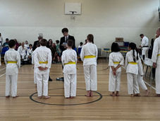Eight yellow-belt karate practitioners receiving feedback on their grading from a black-belt.