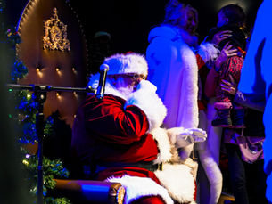 Le Père Noël accueille un enfant sur scène lors de l’événement du 14 décembre, entouré de la Mère Noël et de familles, dans une ambiance chaleureuse et festive remplie de magie et d’émotion.