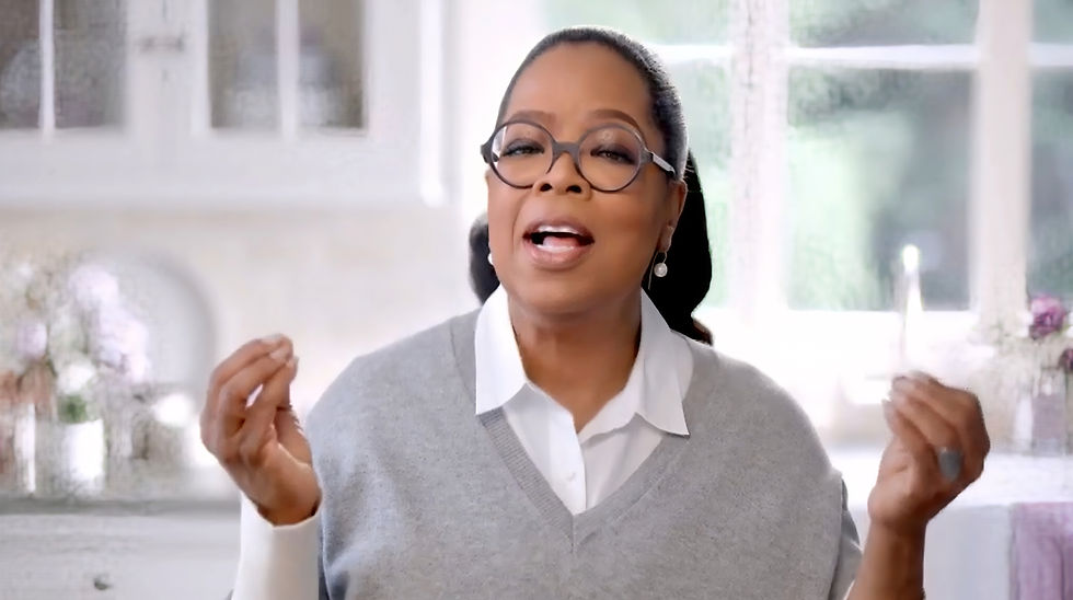 Oprah Winfrey smiling and gesturing in a home setting for O That’s Good commercial.