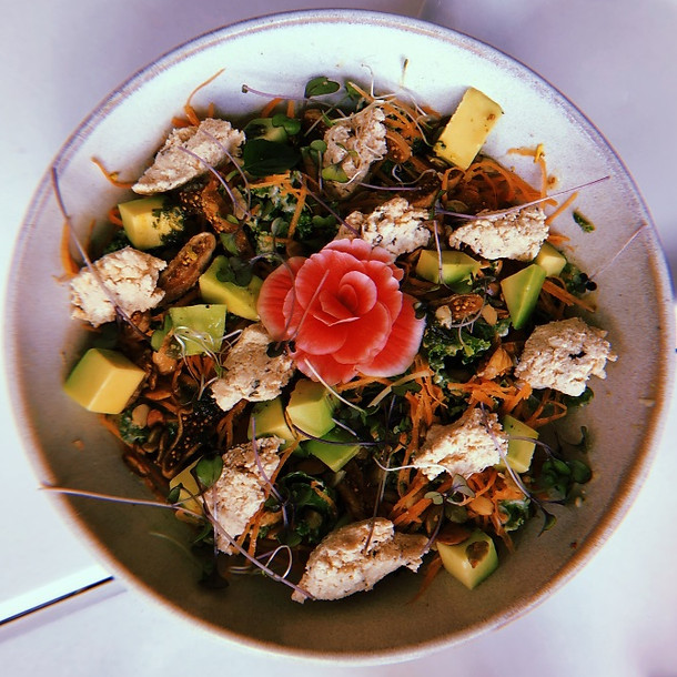 Prato de cerâmica, rústico, com refeição vegana, comida colorida, receita vegana, alimentação saudável, tofu, abacate, cenoura, brócolis, broto de alfafa, com flor decorativa de cor rosa ao centro
