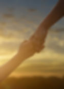 Helping hands reaching toward sunset hope