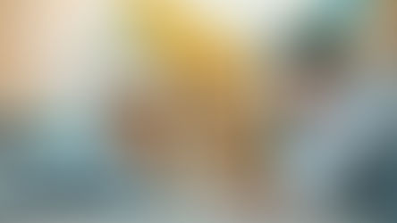 Father and son lie on a striped rug, smiling at each other. Bright shelves with plants and decor are visible in the colorful background.