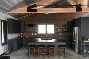 Industrial kitchen with black cabinets and brick wall.