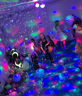 Barn i barnebursdag danser i et rom fylt med diskolys og ballonger.