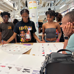 four students engaged around a table editing large colorful posters 