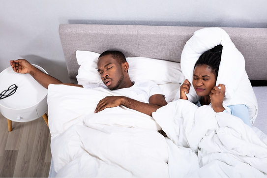 man snoring and wire with pillow over her ears in bed