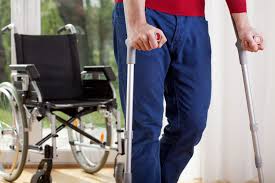 Man walking with crutches with a wheelchair nearby