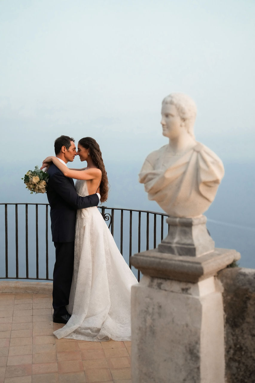 Pietro and Marina embrace on the panoramic terrace of Villa Cimbrone, with the azure sea of the Amalfi Coast in the background