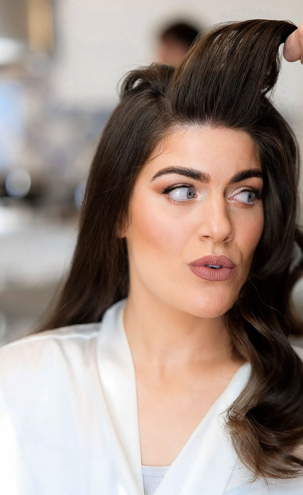 Bride having her hair styled, soft morning light capturing calm and anticipation.