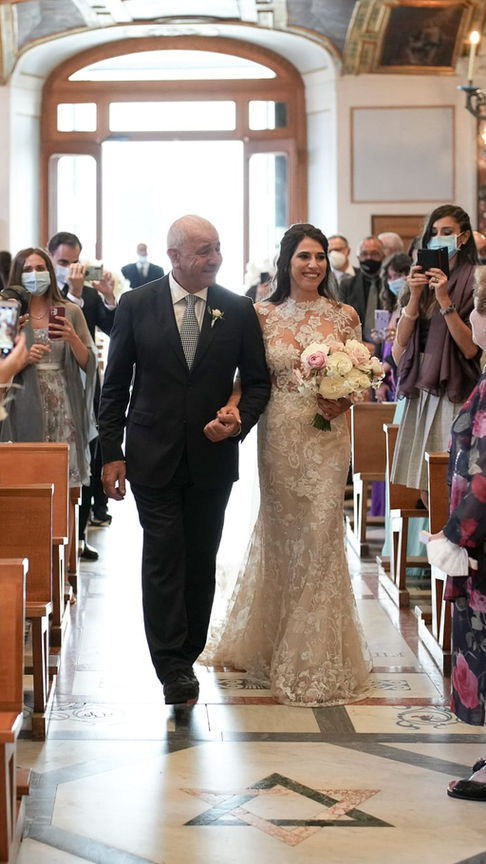 Bride walking down the flower-lined church aisle, radiant and graceful in the golden light.