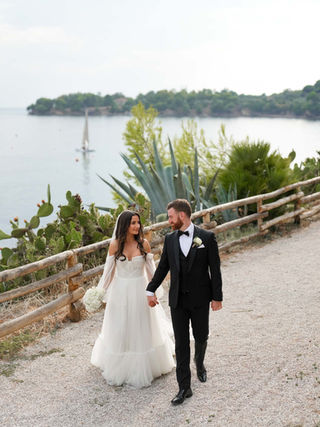 Bride and groom walking along the coastal promenade of Santa Maria di Castellabate, framed by the Tyrrhenian Sea and golden morning light.