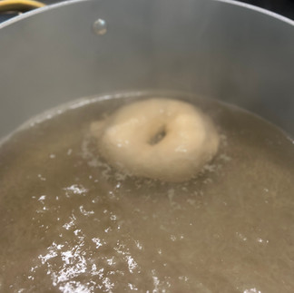 Single sourdough bagel boiling in water showing the crust forming