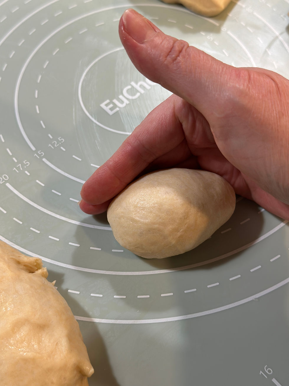 Hand cupping a sourdough dough ball against a silicone baking mat to create surface tension during shaping