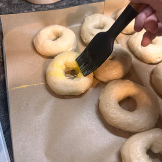 Brushing egg wash onto sourdough bagels on a parchment lined baking sheet