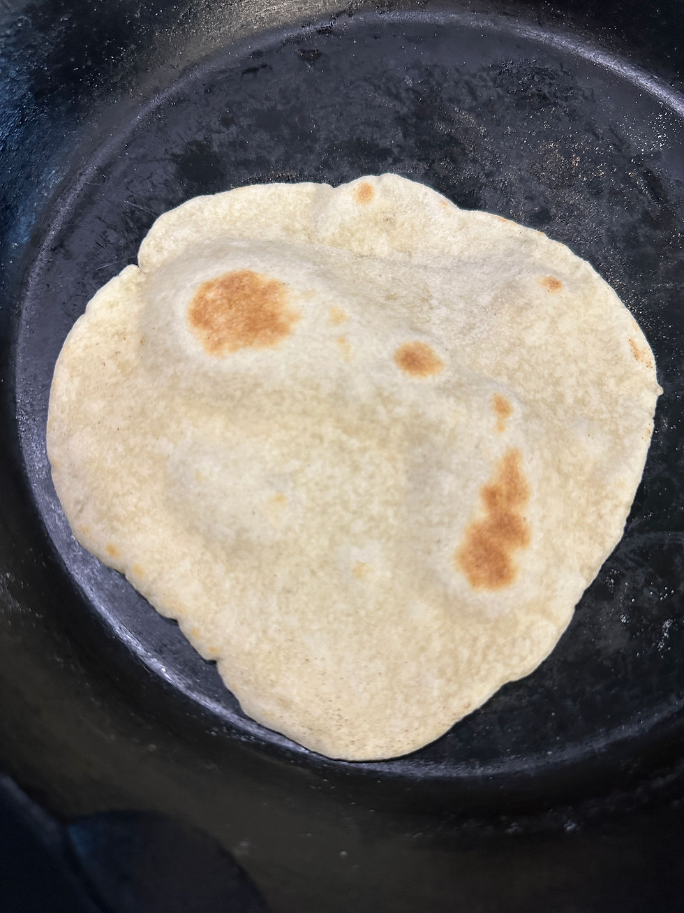 Sourdough flour tortilla with golden brown cook marks on a dry cast iron skillet, overhead view