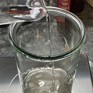 Filtered room temperature water being poured into a Weck jar over sourdough starter on a kitchen scale