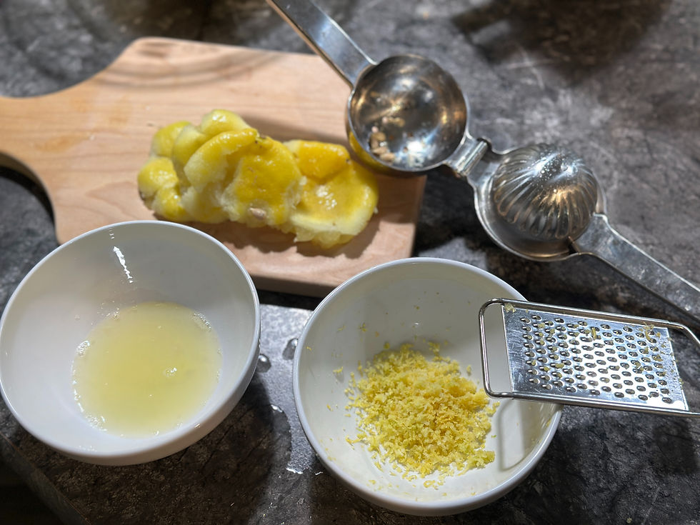 Fresh lemon juice and lemon zest in small white bowls with a citrus juicer and squeezed lemon halves on a cutting board