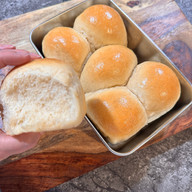 Holding Sourdough Hawaiian Roll Beside Pan of Rolls
