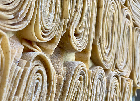 Rolled pasta sheets stacked high; close-up view of fresh Tortello.