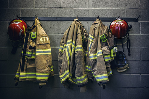 firefighter coats and helmets hang along a wall