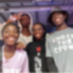 Four smiling people pose indoors, one making a peace sign.