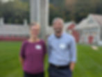 Two people smiling outdoors with name tags, in front of a farm backdrop.
