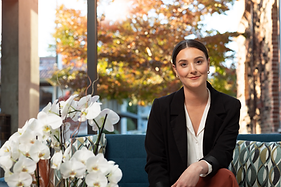 Rachelle Wang, Rental Specialist wearing a dark blazer siting on a sun lit porchnext to white orchids