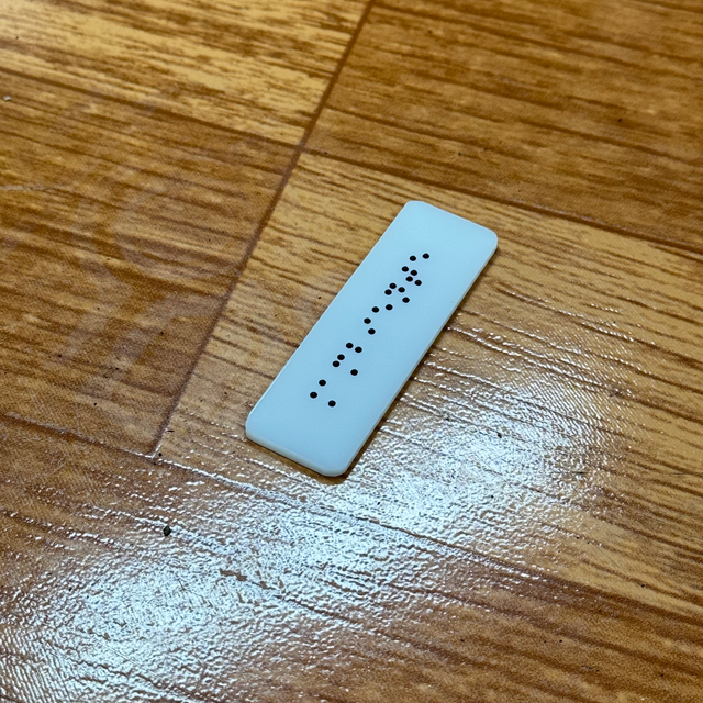Placa pequeña de acrílico blanco con una línea de braille negro, vista en ángulo