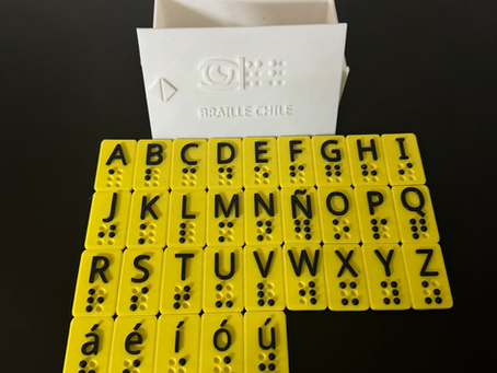 Abecedario braille impreso en 3D: fichas amarillas con la letra en negro y su signo braille en puntos negros, de la A a la Z con Ñ y vocales con tilde, delante de una caja blanca con el logo de Braille Chile.