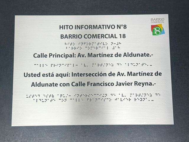 Placa de acero "Hito informativo N°8, Barrio Comercial 18" con calle principal Av. Martínez de Aldunate y braille