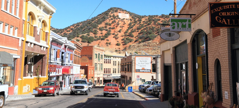 Historic storefronts and brick buildings along Main Street in Bisbee, Arizona, with the red rock mountain in the background.