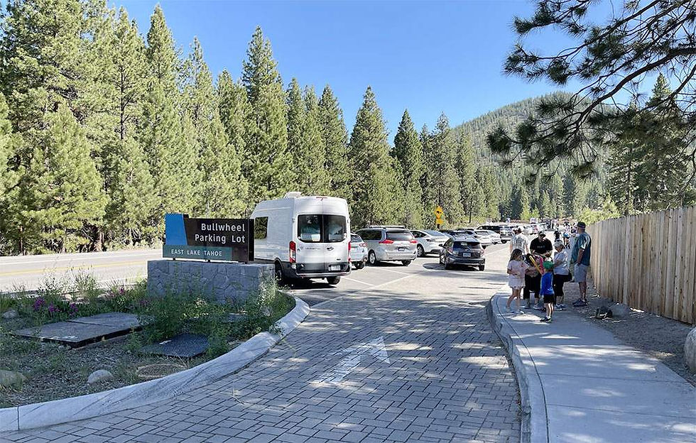 Bullwheel Parking Lot sign at East Lake Tahoe with parked vehicles, tourists on the sidewalk, and surrounding pine trees.