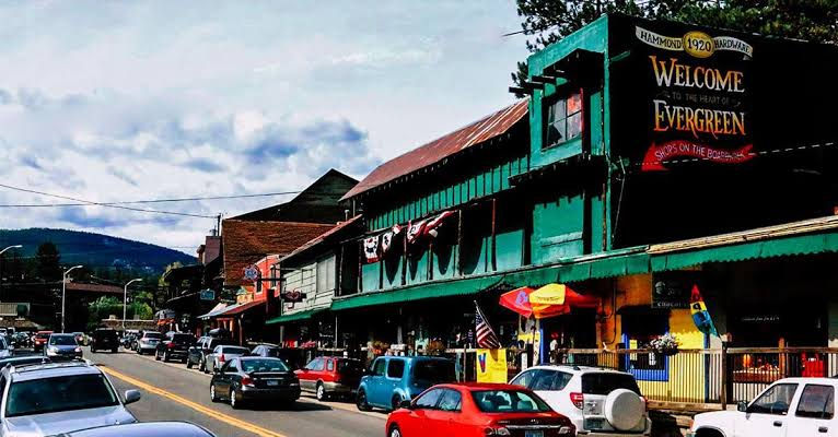 Historic downtown Evergreen, Colorado, showing street-side shops, parked cars, and a painted sign welcoming visitors to the heart of town