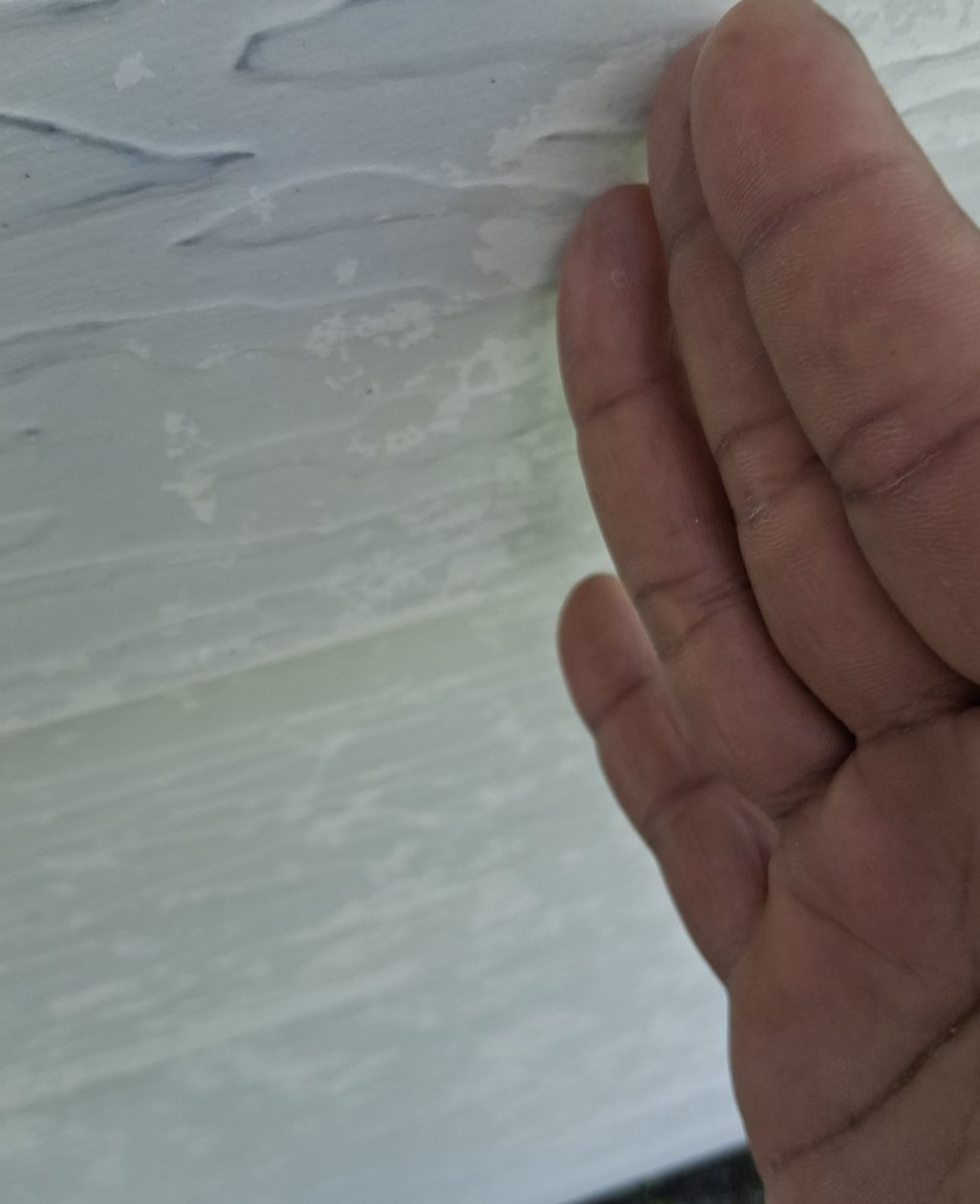 Close-up of a hand checking chalk transfer on a painted aluminum siding test area
