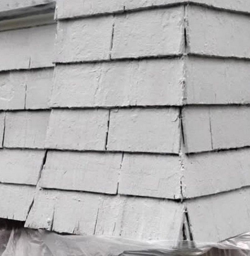 Close-up of cracked and deteriorated painted wood shingles in an anonymized exterior project