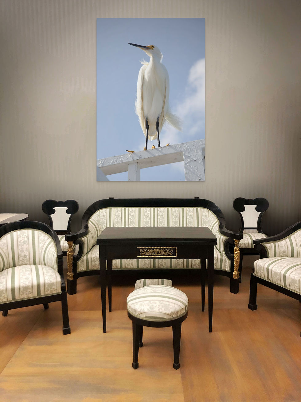 Elegant room with striped furniture and a dark wood table. A large photo of a white Egret perched on a beam against the sky is on the wall in Living Room Area.