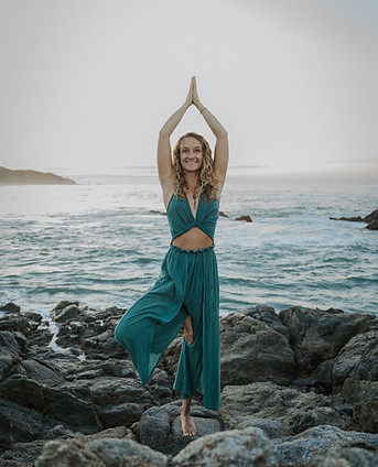 Vrouw in boomhouding op rotsen aan zee tijdens een yogasessie van Energy Source in Alkmaar – balans en aanwezigheid in de natuur.