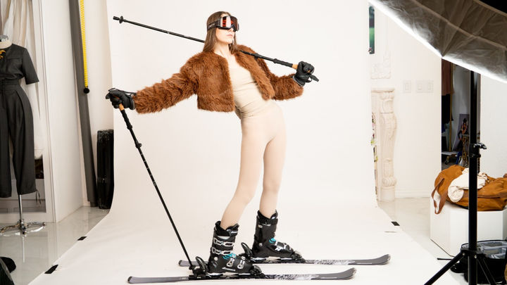 Model in a faux fur jacket and ski boots posing with ski poles for the brand Base 2 Peak winter apparel campaign.