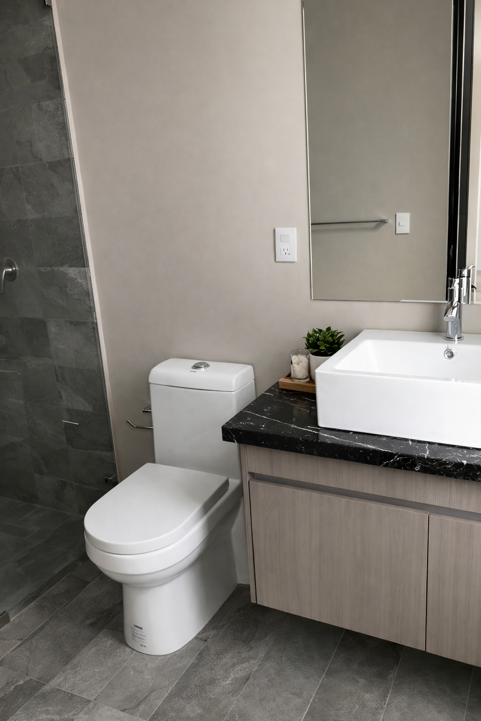 Modern bathroom with dark stone vanity, wood cabinetry, and contemporary fixtures.