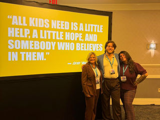 Three conference speakers, including Kelly Tanner, smiling and posing together in a conference room in front of a projection screen displaying the quote: 'All kids need is a little help, a little hope, and somebody who believes in them.' — Earvin 'Magic' Johnson.