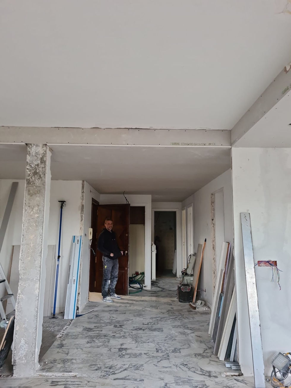 Homme debout dans un couloir en rénovation, Peintre en bâtiment, menuiserie, Oj Service.