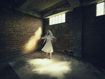 Photo : Cédric Brison. Une femme en robe et voile blancs tournoie dans une pièce au décor brut et vide.