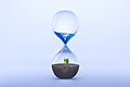 Hourglass with fresh water drop to green plant planting on dry land isolated background, m