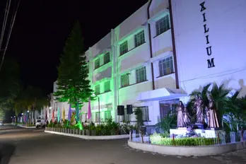 Illuminated "XILIUM" building at night with green and blue lights, statue garden.