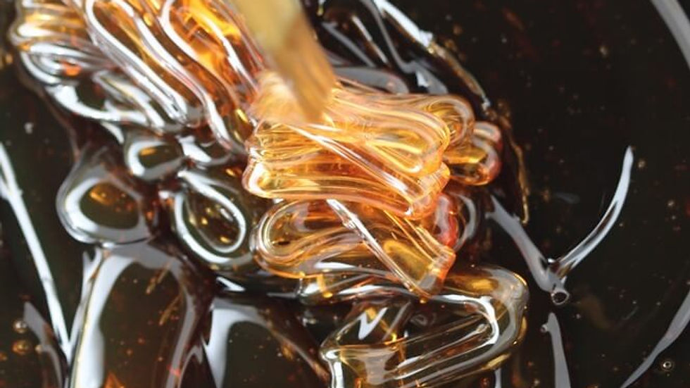 Gros plan d’un filet de miel doré se mêlant à un liquide noir brillant, avec des volutes luisantes.