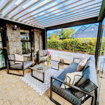 Louvred pergola roof with glass walls over outdoor lounge seating beside a natural stone wall