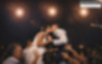 Bride lifted by the groom during a joyful nighttime wedding celebration with guests and warm lights